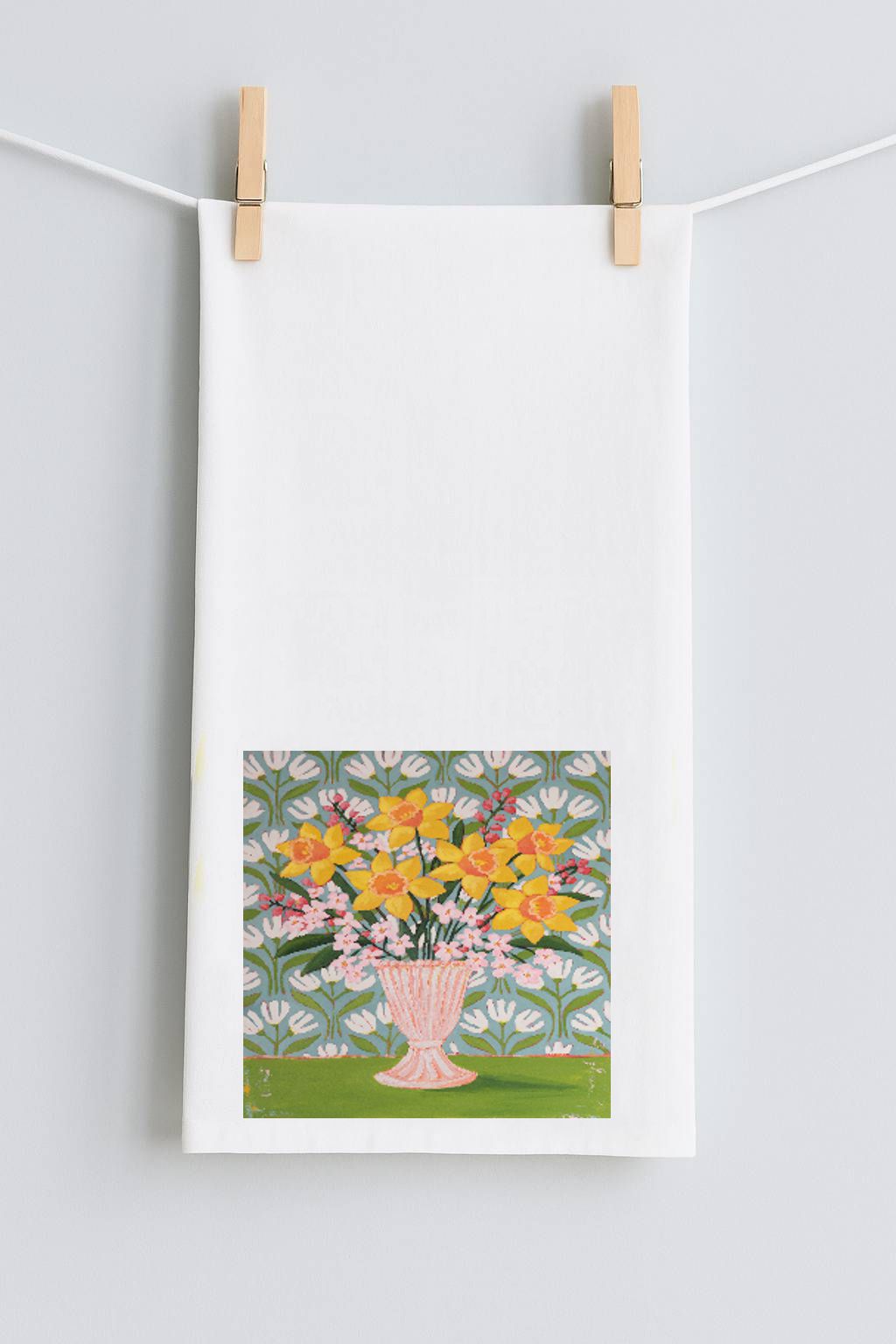 Framed artwork of a floral design hanging on a string with wooden clips against a light gray background.