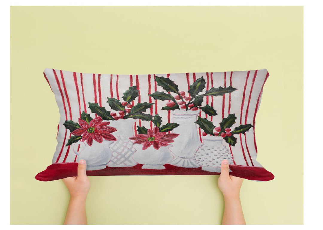 Decorative pillow with poinsettias and holly on a striped background held by hands against a yellow background