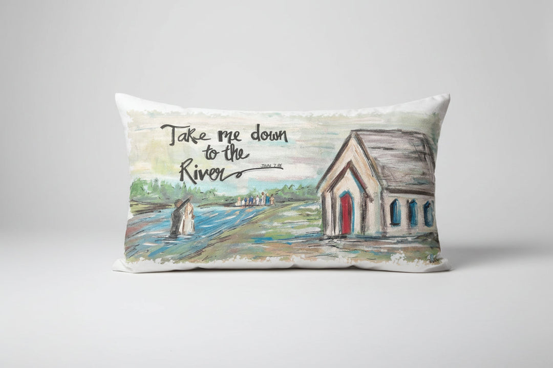 A rectangular lumbar pillow with an artistic depiction of a river scene and a church, with the text 'Take me down to the river'.